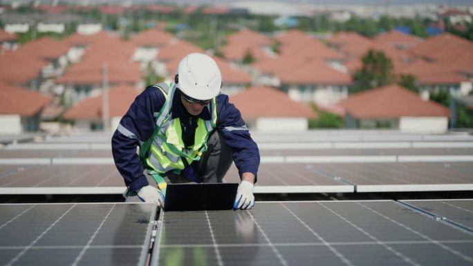 穿制服的工程师在屋顶用手提电脑检查太阳能板。