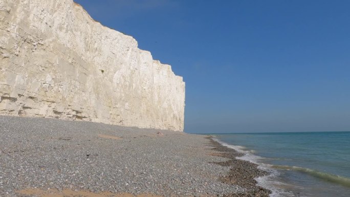 令人难以置信的壮观的白色悬崖矗立在蓝色的海洋旁的岩石海滩上
