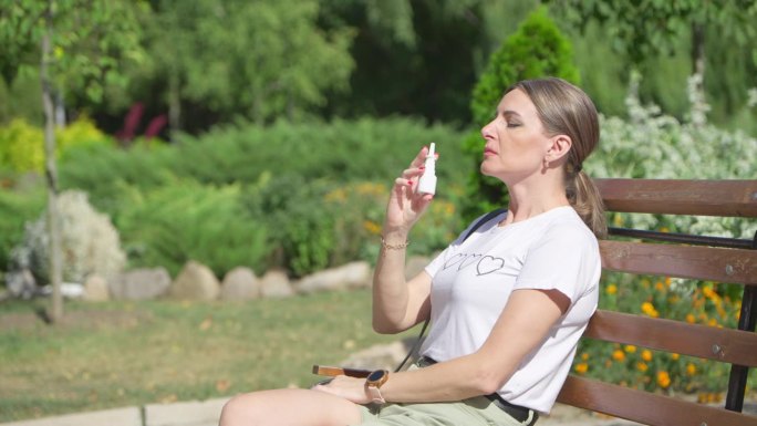 一位中年妇女坐在公园的长椅上使用鼻腔喷雾剂。