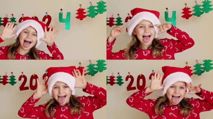有趣，兴奋，快乐的学步女孩穿着圣诞服装，红色圣诞老人帽装饰冬季度假屋，手工纸花环数字2024。孩子们
