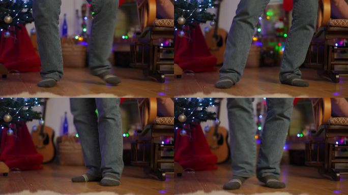 在圣诞树附近的镶木地板上，穿着牛仔裤和袜子跳舞的腿的特写。