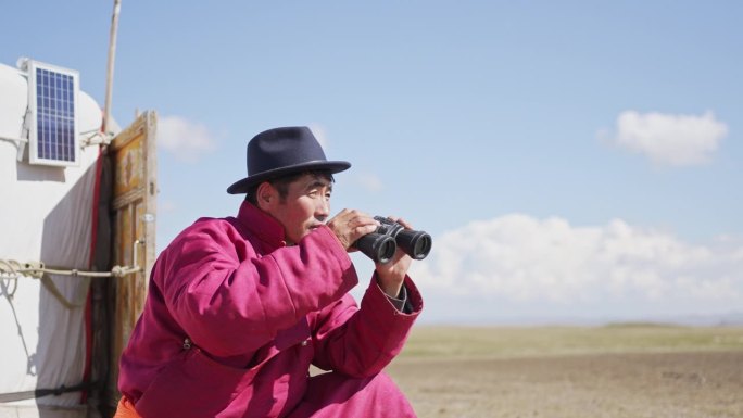 一个蒙古游牧民族正在用双筒望远镜观察羊群