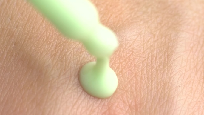 绿色保湿精华液在移液管中落在非常干燥的皮肤上。护肤化妆品。柔和的绿色的精华滴从移液器滴在女人的手干燥