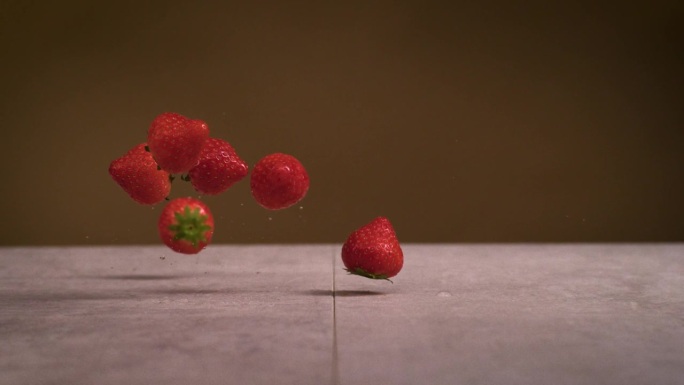 草莓落在石头表面，棕色背景，超级慢动作
