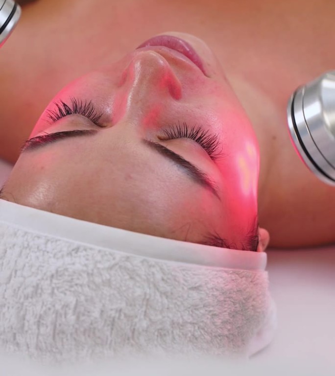 顾客在现代美容院接受LED红光面部护理，以恢复皮肤活力。抗衰老，胶原蛋白促进，痤疮治疗疗程与非侵入性
