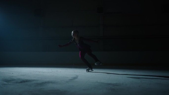 有动力的未来冠军女孩，有才华的少年花样滑冰运动员在黑暗中的溜冰场训练