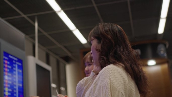 两名年轻的亚洲女子在机场查看电子登机板，查询航班、登机门和登机时间。