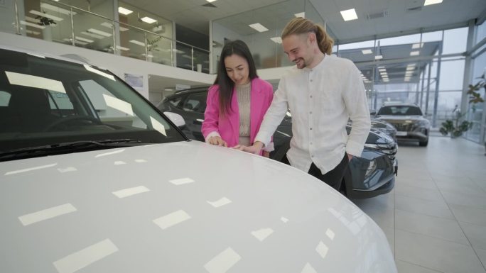 漂亮的年轻夫妇在汽车展示厅挑选新车。