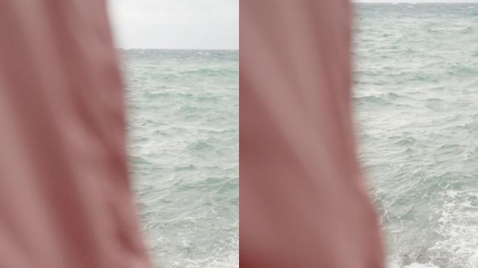 垂直视频。从一件粉红色连帽雨衣后面的第三人称视角，一个人观察海上的风暴和巨浪。慢动作。