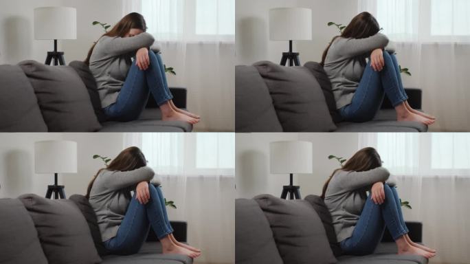 不快乐的焦虑年轻的白人女子用膝盖遮住脸坐在家里客厅的沙发上，伤心欲裂的女性在抑郁中感到绝望和焦虑，有