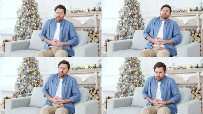 一名心烦意乱的男子在冬季新年圣诞假期坐在家里客厅的沙发上感到胃痛