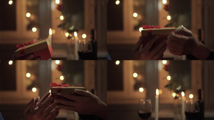礼物，情人节，周年纪念。在浪漫的晚餐氛围中，在美丽的灯光和烛光的背景下，礼物在手中传递