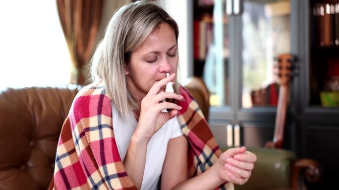 一位女士坐在家里的沙发上使用鼻腔喷雾剂