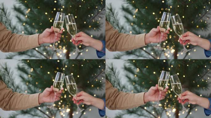 男人和女人的手优雅地举起香槟酒杯敬酒，冒着泡沫，在装饰精美的圣诞树前，一起庆祝新年。