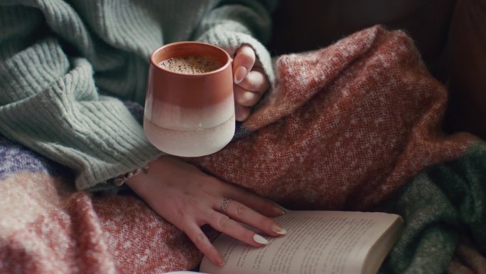 一个女人在家里穿着冬天的套头衫，在杯子里喝着温暖的热咖啡
