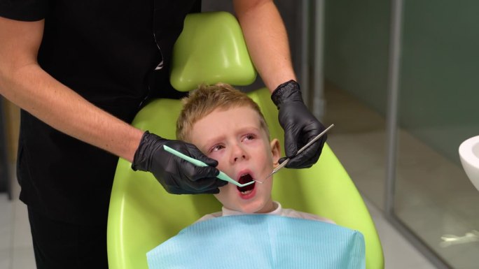 悲伤的小男孩在牙医治疗牙齿时张大了嘴巴。孩子不敢治牙