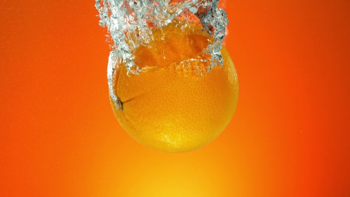 整个橙子落入水中的超级慢动作，孤立在橙色背景上。