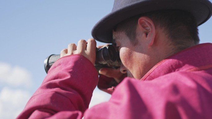 一个蒙古游牧民族正在用双筒望远镜观察羊群
