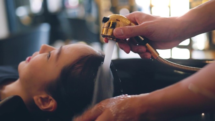 特写——美发师在美容院的水槽里用干净的水和洗发水洗女人的黑头发。