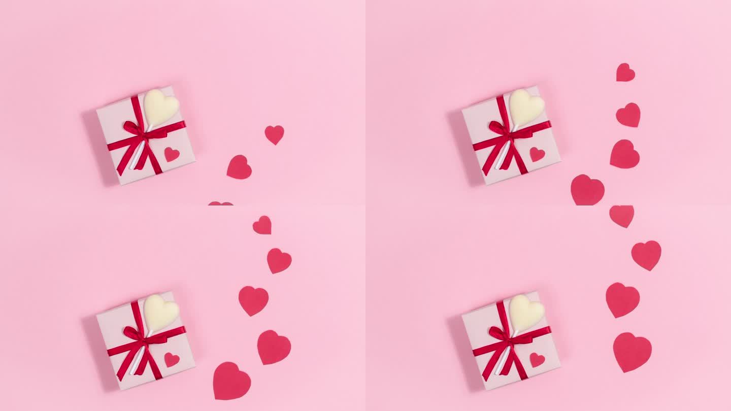 粉色礼盒旁系着红丝带和白色巧克力心形糖果，爱心飞逝，象征着爱。情人节贺卡。