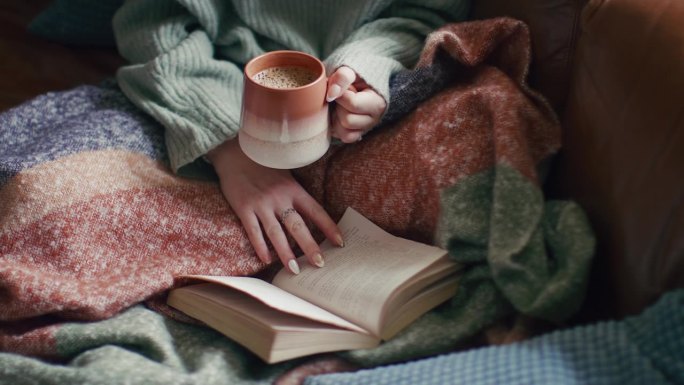 一个女人在家里穿着冬天的套头衫，在杯子里喝着温暖的热咖啡