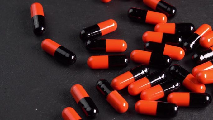 许多黑色和橙色药丸胶囊或抗抑郁药倒在黑色的宏板上。止痛头痛的药物或药物。制药行业