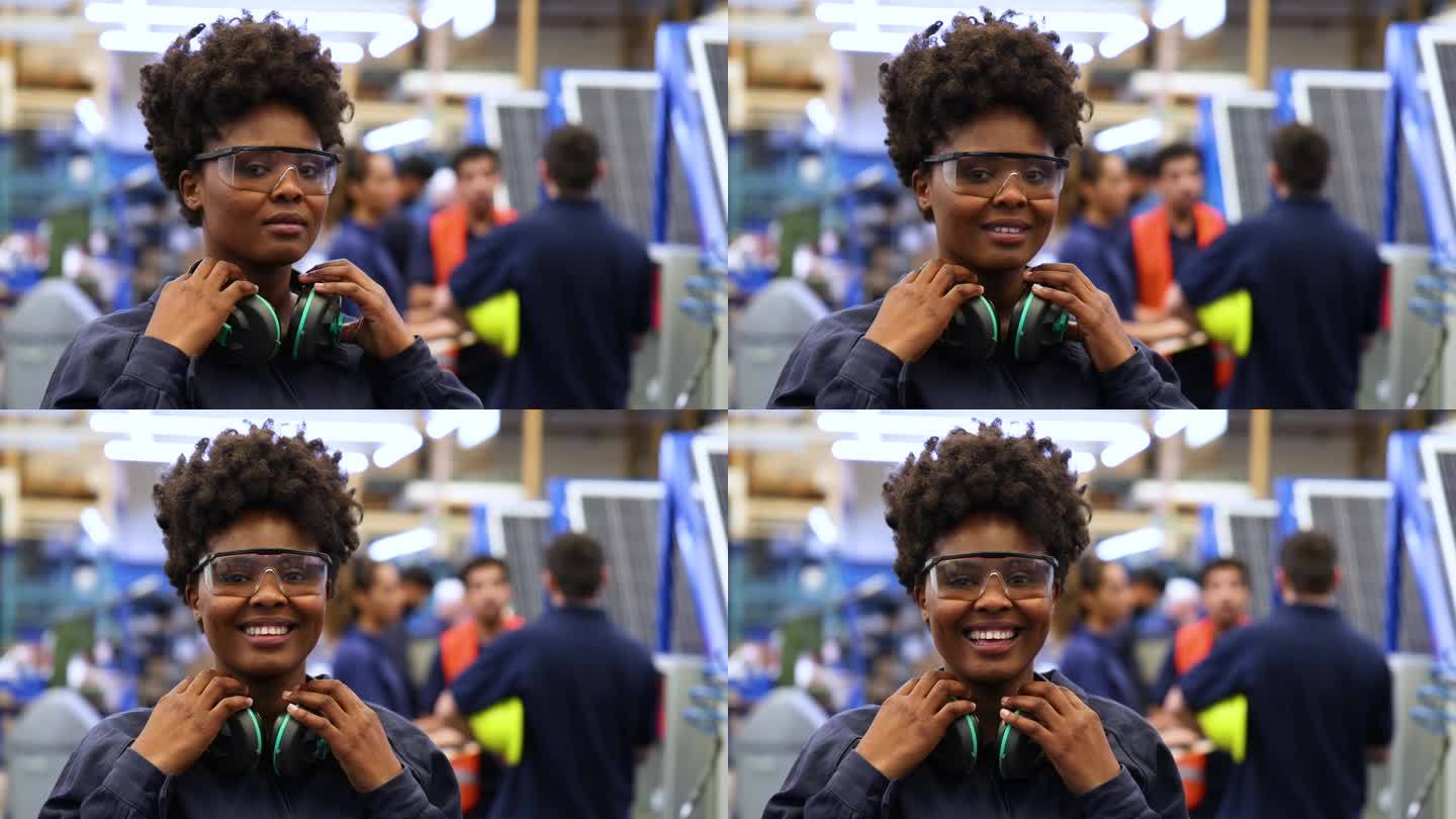 一名黑人女工戴着护目镜和护耳，对着镜头微笑