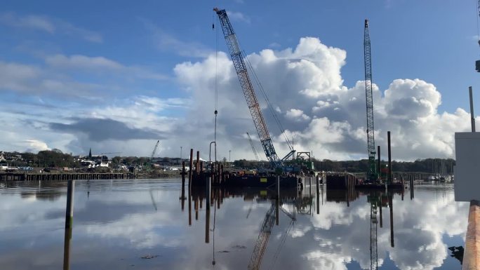 在爱尔兰沃特福德，在一个平静的冬季早晨，在涨潮时，苏尔河上的施工驳船正在为横跨苏尔河的新人行桥打桩
