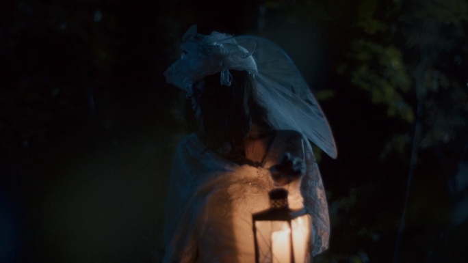 一位身穿白衣的妇女在夜晚提着一盏旧灯笼