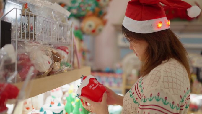 年轻的亚洲妇女戴着圣诞老人的帽子为圣诞节挑选圣诞礼物。女士在挑选圣诞装饰用品。圣诞节的庆祝活动。圣诞