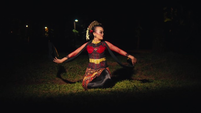 在森林里，一位亚洲妇女坐在绿色的草地上，用手和红色的围巾跳舞