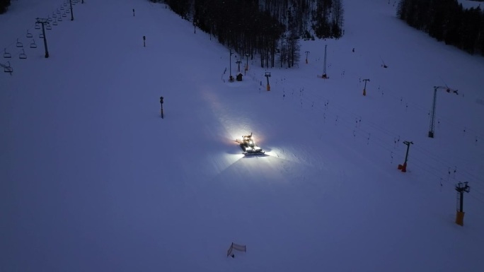 在斯洛文尼亚克拉尼斯卡戈拉的冬夜，在积雪的高山滑雪坡上工作的雪车鸟瞰图。无人机俯瞰雪车梳理雪，滑雪胜
