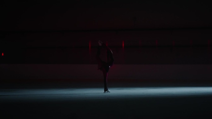 神秘的轮廓才华横溢的女花样滑冰运动员在溜冰场在黑暗中，专业冰上表演