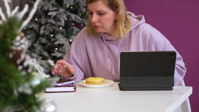 圣诞节期间在线工作。年轻开朗的金发女郎，穿着温暖的连帽衫，坐在舒适的咖啡馆里，用笔记本电脑和朋友聊天