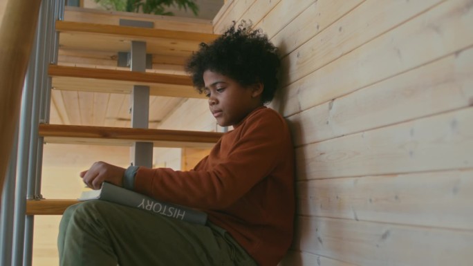 非裔美国男孩和书坐在楼梯上