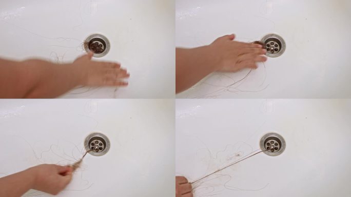 人的手用努力拉出大量的头发，堵塞了浴缸的排水管。水管堵塞。