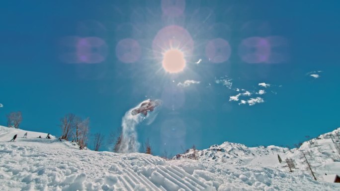 SLO MO滑雪板运动员在阳光明媚的日子里练习特技。男子正在雪山上玩单板滑雪。他喜欢冬季运动。