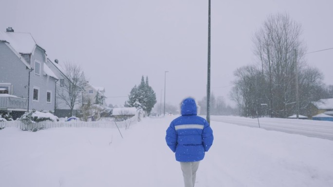一名身穿蓝色外套的女子欣赏真正的冬季童话，她走在斯堪的纳维亚村庄的街上，大雪纷天