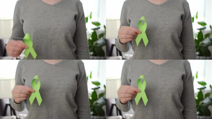 站在房间里的女性手拿着小石灰绿丝带的特写。失弛缓症，精神健康，非霍奇金淋巴瘤，莱姆病意识，世界肾脏日