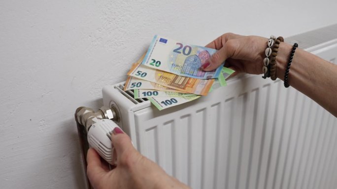 女人手里拿着欧元钞票，在家调节暖气片的温度