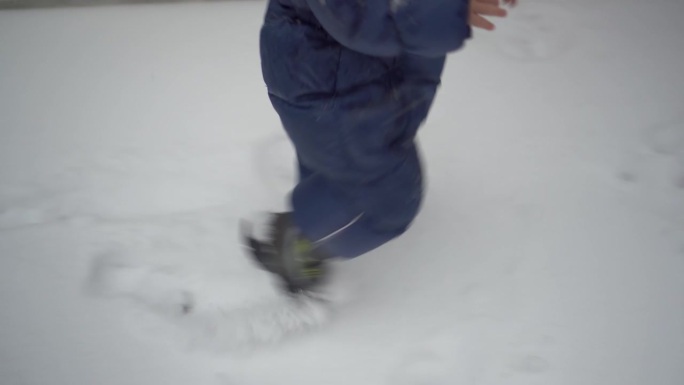 一个小孩走过刚下过的雪。一个穿着羽绒服的男孩踩在雪地上留下了脚印。腿收起来。