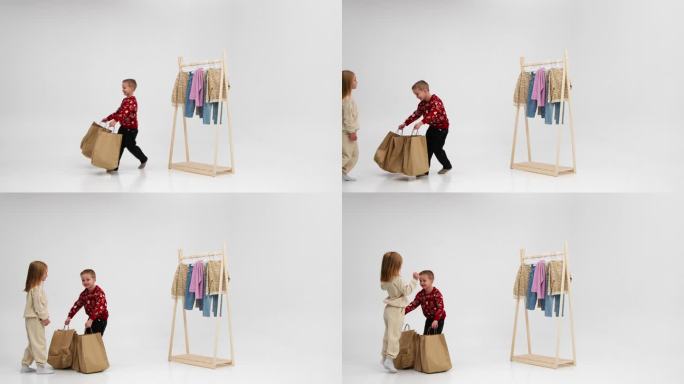 小时尚达人带着浅色背景的包裹。可爱的微笑的小女孩在衣架的背景袋享受购物。童装风格广告理念。