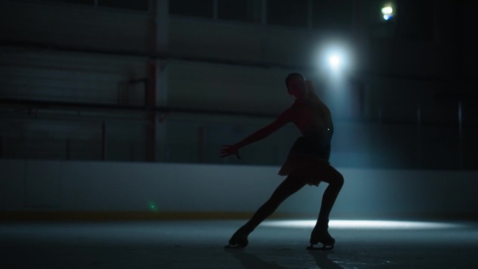 专业花样滑冰女子在黑暗中的冰上优雅的轮廓，浪漫的舞蹈表演