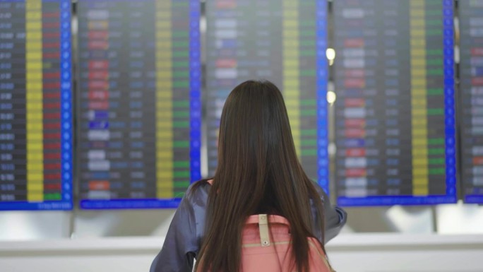 图为，在机场候机楼，站在航班时刻表前看着航班信息牌，用智能手机拍照的年轻亚洲女性
