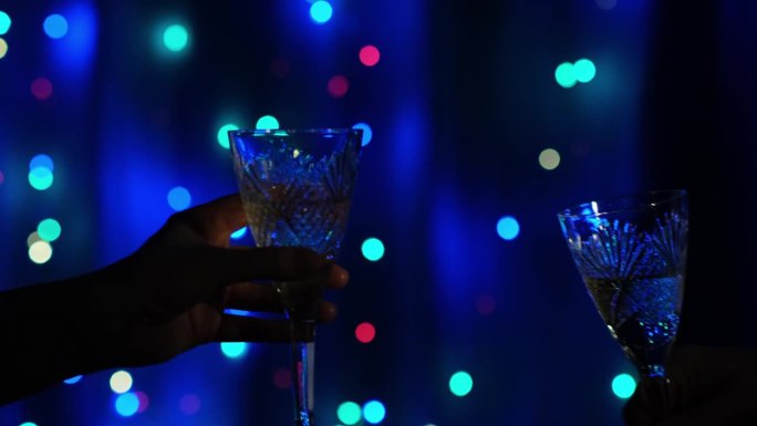 一对叮当作响的水晶酒杯，在闪烁的花环背景上装满了香槟。为新的开始干杯。新年快乐，圣诞快乐。