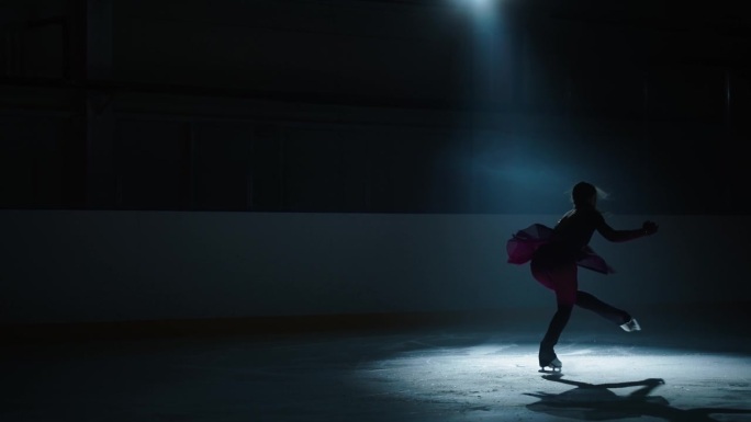 才华横溢的花样滑冰少女在黑暗中跳上冰面，在明亮的灯光下看剪影