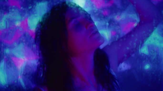 幸福的女孩在湿玻璃后面的霓虹灯下跳舞