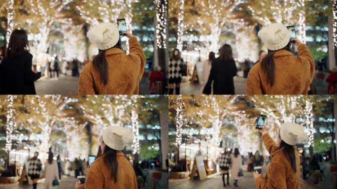 一名女游客在寒冷的圣诞夜用手机拍摄城市街道的装饰和灯光。