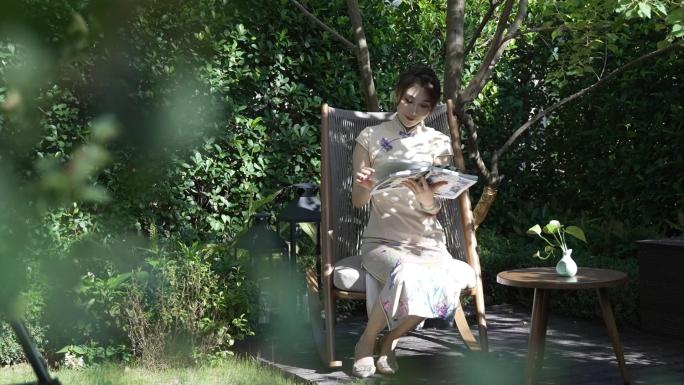 穿旗袍的美女在阳光明媚的凉亭树荫下看书