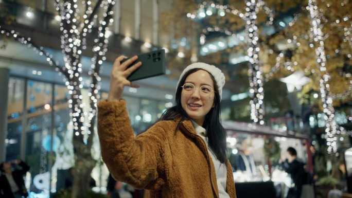一个快乐的女人在美丽的圣诞夜用手机拍照。